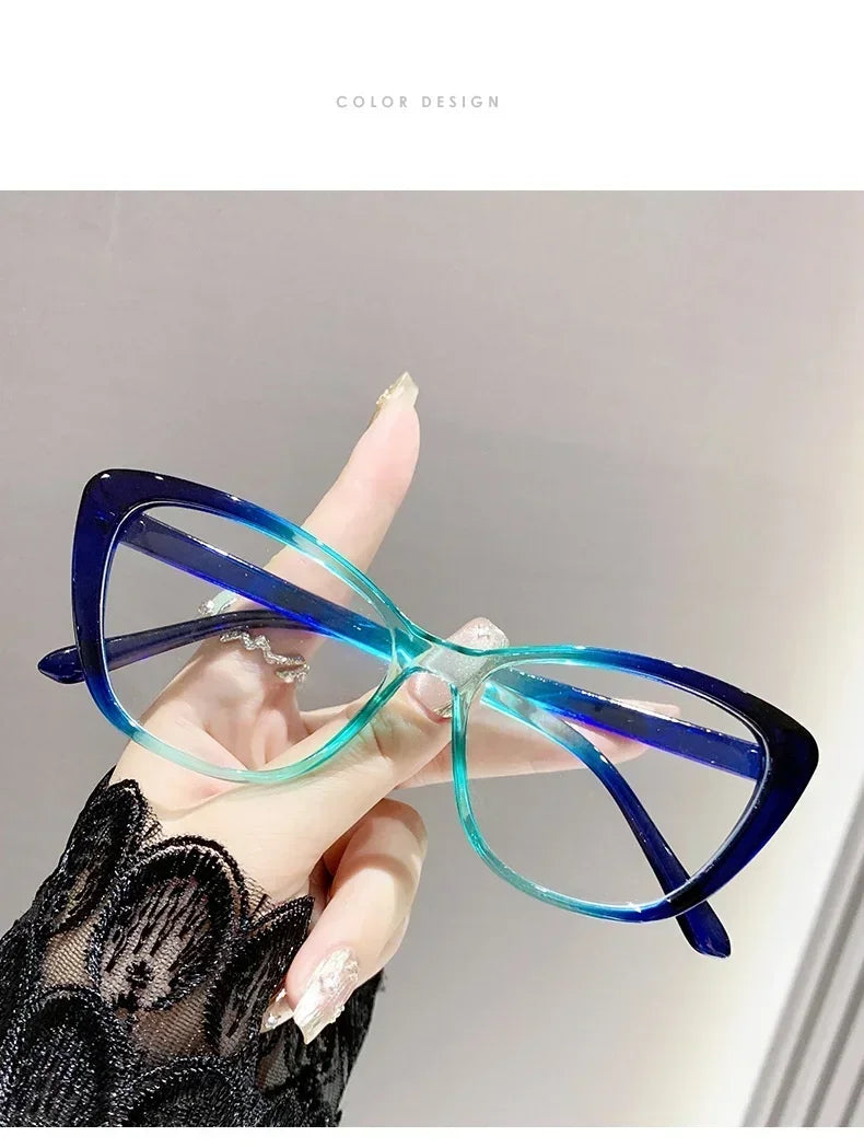 A hand holds a pair of blue-tinted cat eye reading glasses against a light background.