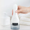 Una mano sostiene un exfoliador eléctrico blanco y un dispositivo con inserto de grano oscuro en un recipiente transparente.