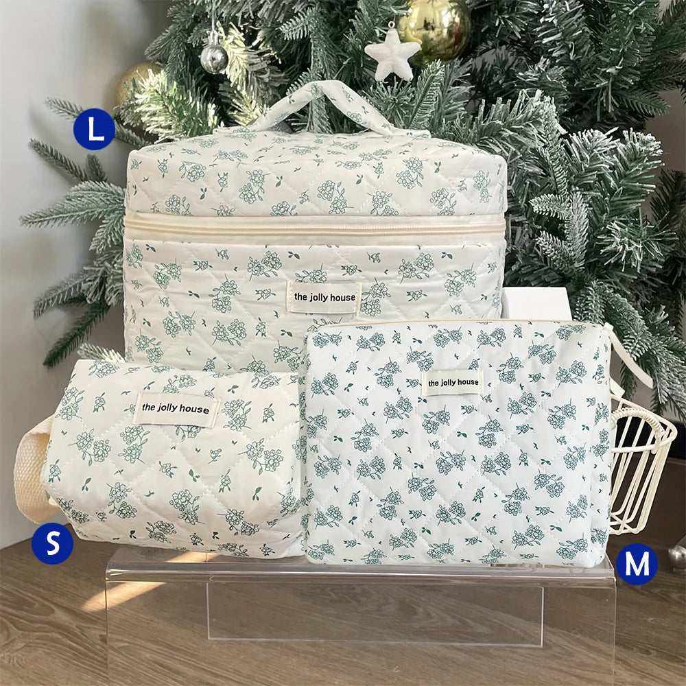 A white quilted cotton makeup bag with a floral pattern displayed in front of a green Christmas tree.