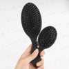 A pair of black matte boar bristle hair extension brushes held in a person's hand.