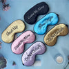 A collection of embroidered silk sleep masks in black, light blue, pink, and gold tones arranged on a light blue surface.