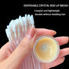 A hand holds a clear glass jar of lip product next to disposable crystal rod lip brushes.