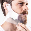 A man is holding a clear plastic beard shaping tool against his face to style his beard.