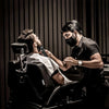 A man is using professional cordless electric hair clippers on another man's beard.