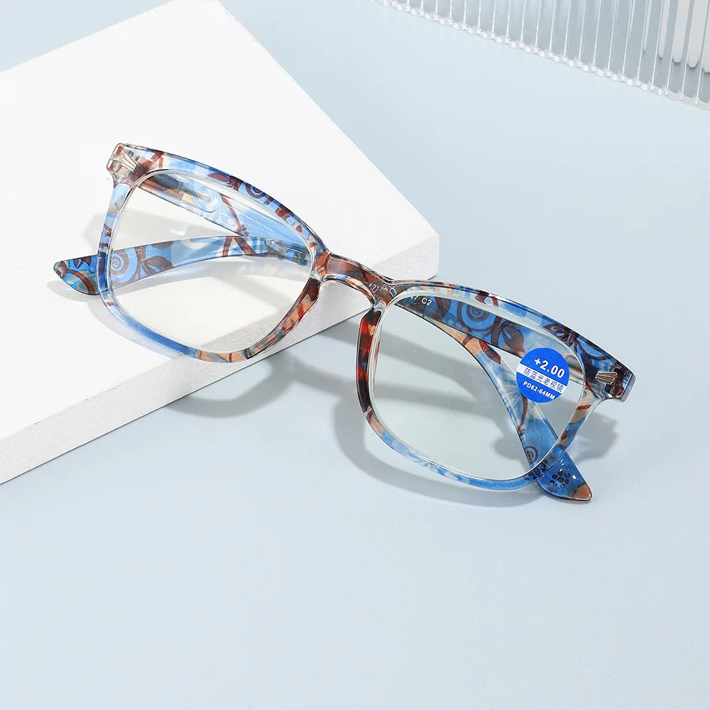 Pair of blue and brown patterned magnifying reading glasses resting on a white surface.