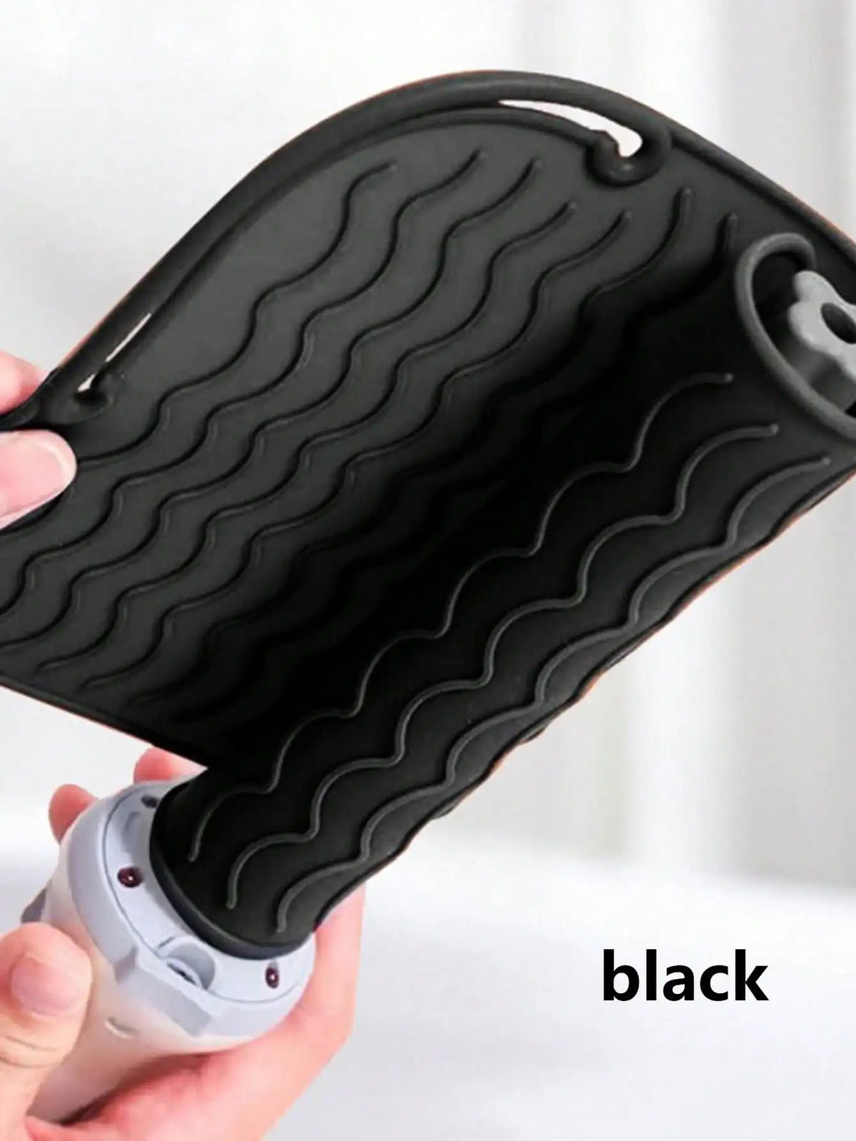 A black silicone heat resistant mat for hair styling tools is being held by a hand.