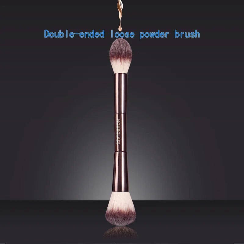 A double-ended loose powder brush with a brown handle and fluffy bristles against a dark background.