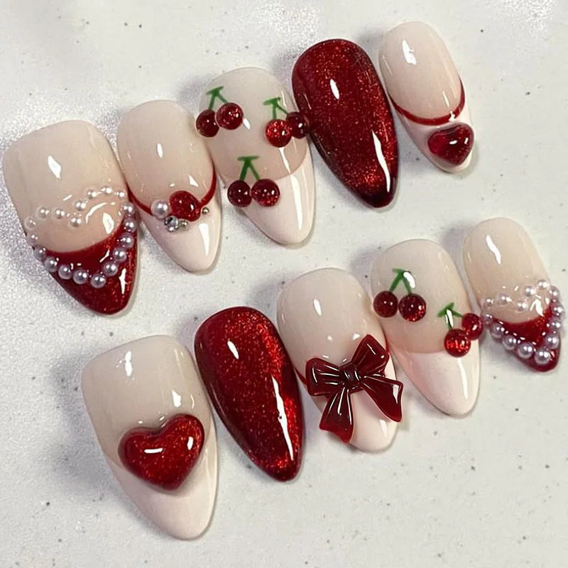 A collection of 24 press-on nails featuring pink and red glitter designs, including hearts, cherries, and pearl accents.