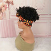 A model wears a black afro puff turban wig with an orange and green patterned fabric in a pink room setting.