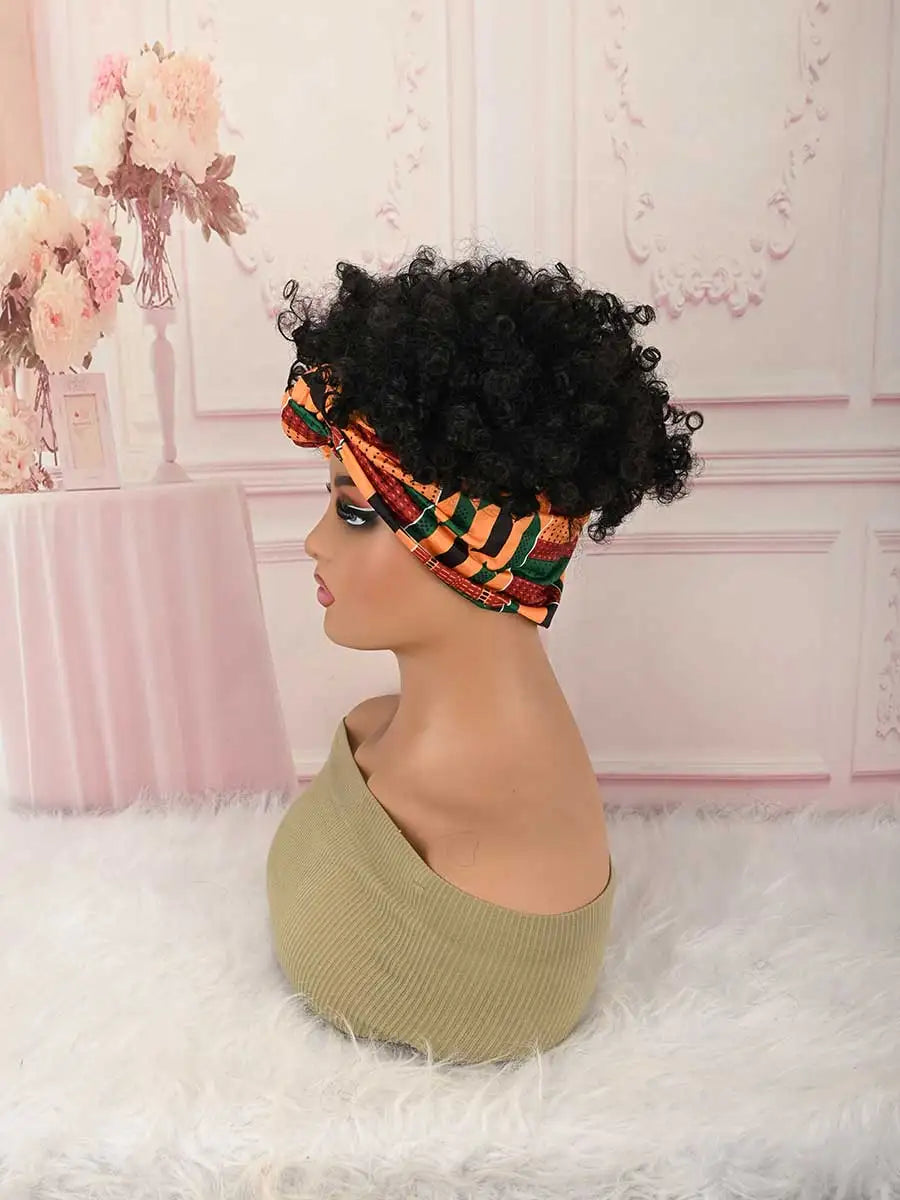 A model wears a black afro puff turban wig with an orange and green patterned fabric in a pink room setting.