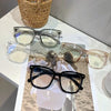 Colección de gafas vintage cuadradas anti-luz azul expuestas sobre una superficie blanca con una cesta tejida de fondo.