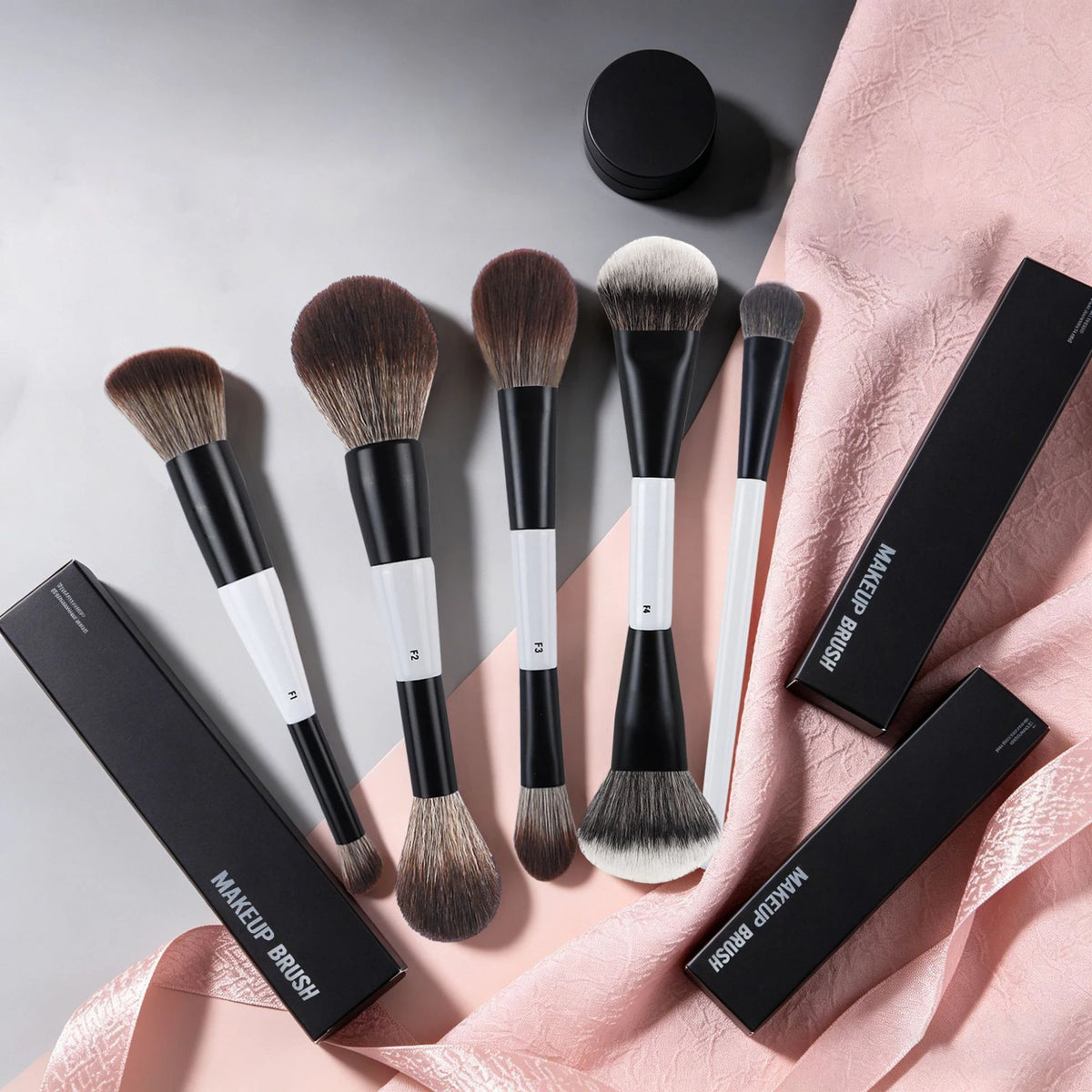 A collection of black and white dual-ended makeup brushes displayed on a pink fabric background.
