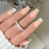 A close-up of a hand displaying white French style press-on nails with coffin shape and a silver ring.