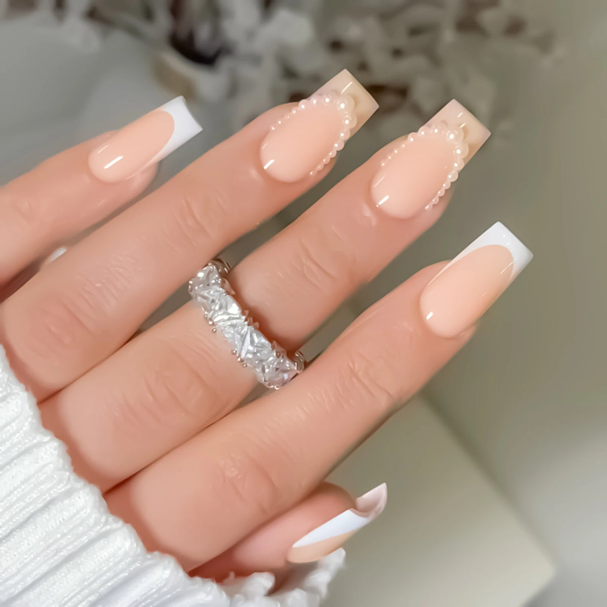 A close-up of a hand displaying white French style press-on nails with coffin shape and a silver ring.