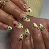 A close-up of a hand displaying elegant press-on false nails with an almond shape featuring delicate floral and ladybug desig