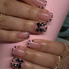 A close-up of a hand displaying nude pink press-on nails with black leopard print and black 3D butterfly charms.