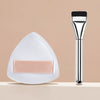 A silver cosmetic foundation puff brush with a white triangular silicone applicator resting on a light surface.