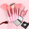 A collection of pink makeup brushes and a compact mirror are displayed on a pink background.
