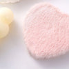 A pink heart-shaped makeup mirror made of soft, fluffy material rests next to a yellow spherical object.