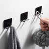 Une main accroche un porte-rasoirs noir sur un mur blanc, avec une serviette grise à proximité.