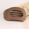 A brown oval flat hair clip with a slotted design is shown resting on a piece of paper.