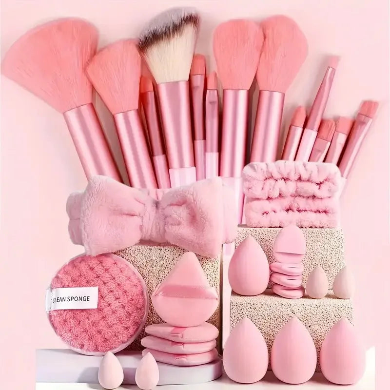 A collection of pink makeup brushes and sponges arranged on a white surface.