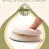 A pink dual-sided makeup sponge puff is shown being used to apply skin concealer on a light green background.