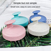 Three colored silicone scalp massage brushes in pink, light blue, and gray resting on green leaves.