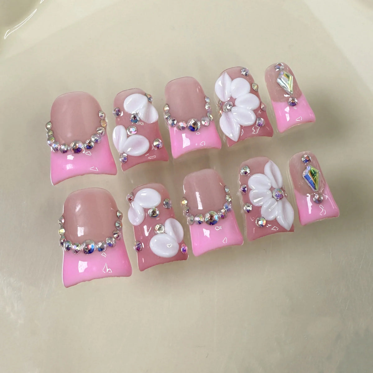 Un set de uñas postizas de perla rosa nude con acentos florales blancos y acabados iridiscentes.