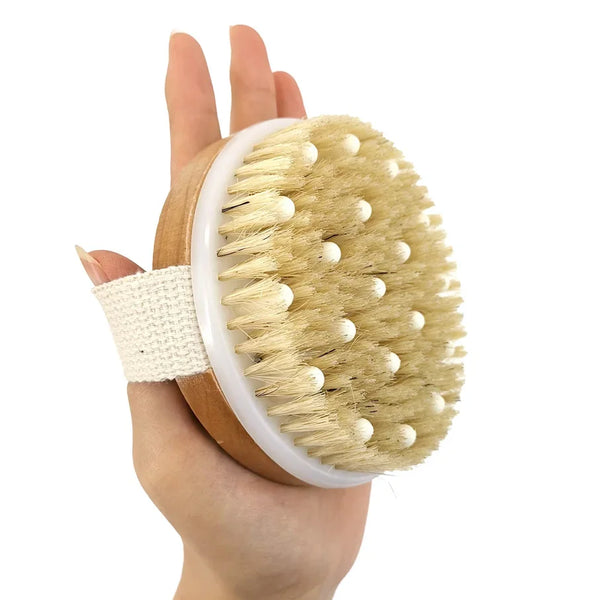 A hand holds a natural bristle body brush with light wood and white accents.