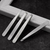 A set of professional stainless steel tweezers lying on a dark surface next to a white frame.
