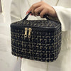 A black knitted canvas makeup pouch with gold zippers is held by a person.