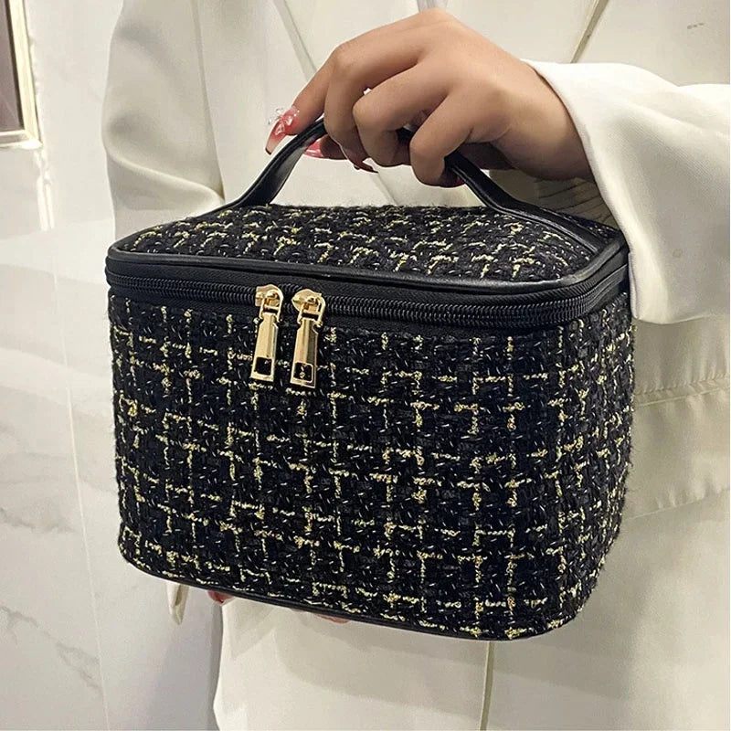 A black knitted canvas makeup pouch with gold zippers is held by a person.