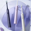 A purple electric toothbrush and a white electric toothbrush are displayed on a light purple surface.