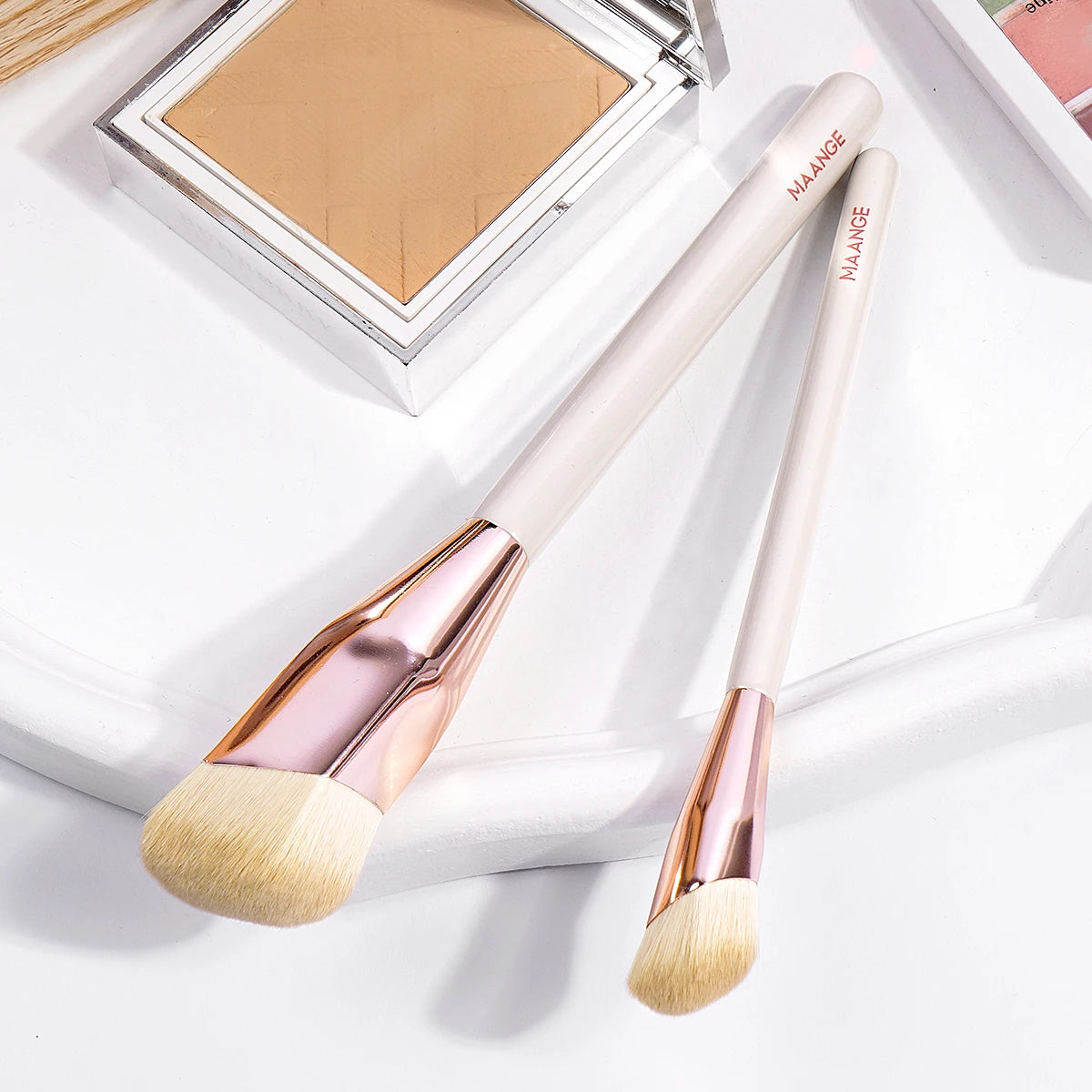 A pair of light pink makeup brushes with rose gold ferrules and natural hair bristles are displayed in a white box.