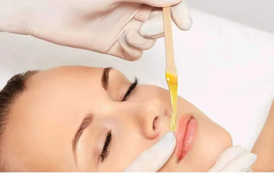 Une main utilise un bâton de dépilation en bois naturel pour enlever les poils de l'arcade sourcilière d'une femme.