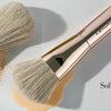 A pink powder and angel blush brush is shown with loose powder on a white surface for natural makeup look.