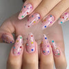 Une main montrant de longues ongles roses et irisants décorés de strass colorés et de paillettes.