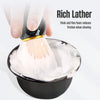 A hand is using a thick, fine foam brush on a black bowl for shaving.