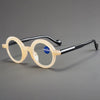 Un par de gafas de lectura con lupa anti-luz azul transparentes con montura negra, apoyadas sobre una superficie gris.