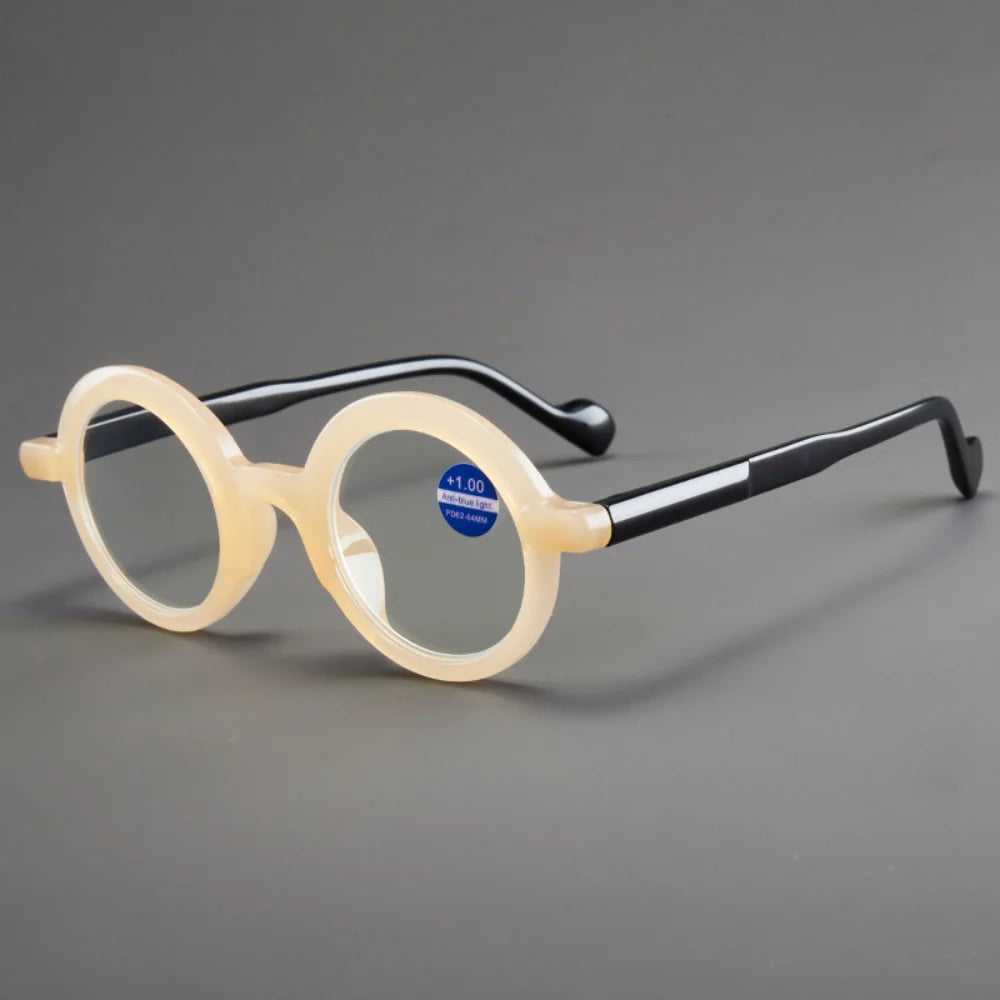 Un par de gafas de lectura con lupa anti-luz azul transparentes con montura negra, apoyadas sobre una superficie gris.