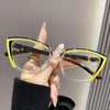 A hand holds a pair of yellow-framed cat eye reading glasses with clear lenses against a light background.