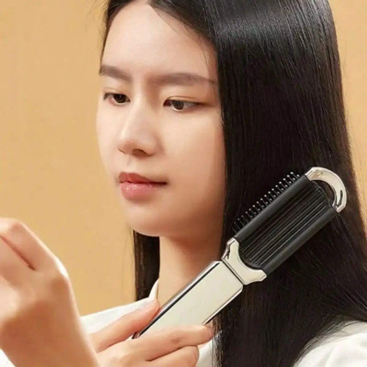 A woman is using a portable compact comb with an airbag and mirror to style her long, dark hair.