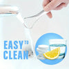 A hand uses a portable stainless steel tongue scraper to clean teeth, with an orange slice and water visible nearby.