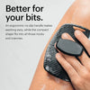 A hand is using a black silicone body scrubber on an arm, demonstrating its ergonomic design.