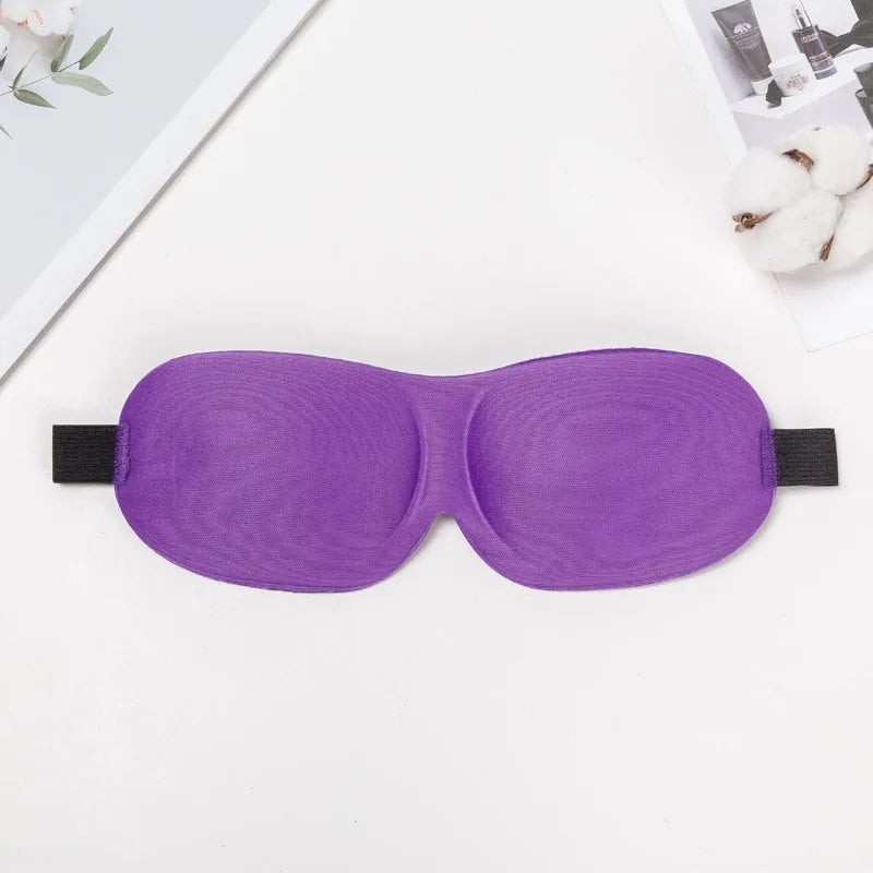 Purple 3D sleep mask for light blocking lying on a white surface.