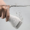 Una mano sostiene un exfoliador y limador eléctrico blanco bajo el agua corriente.