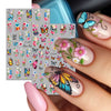 A hand displays fingernails decorated with floral and butterfly nail stickers for DIY decoration.