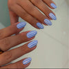 Close-up of a hand displaying reusable fake nails with almond shaped tips painted in blue and white stripes.