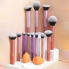 Una colección de doce brochas de maquillaje profesionales en varios tonos de rosa y púrpura exhibidas sobre una superficie bl